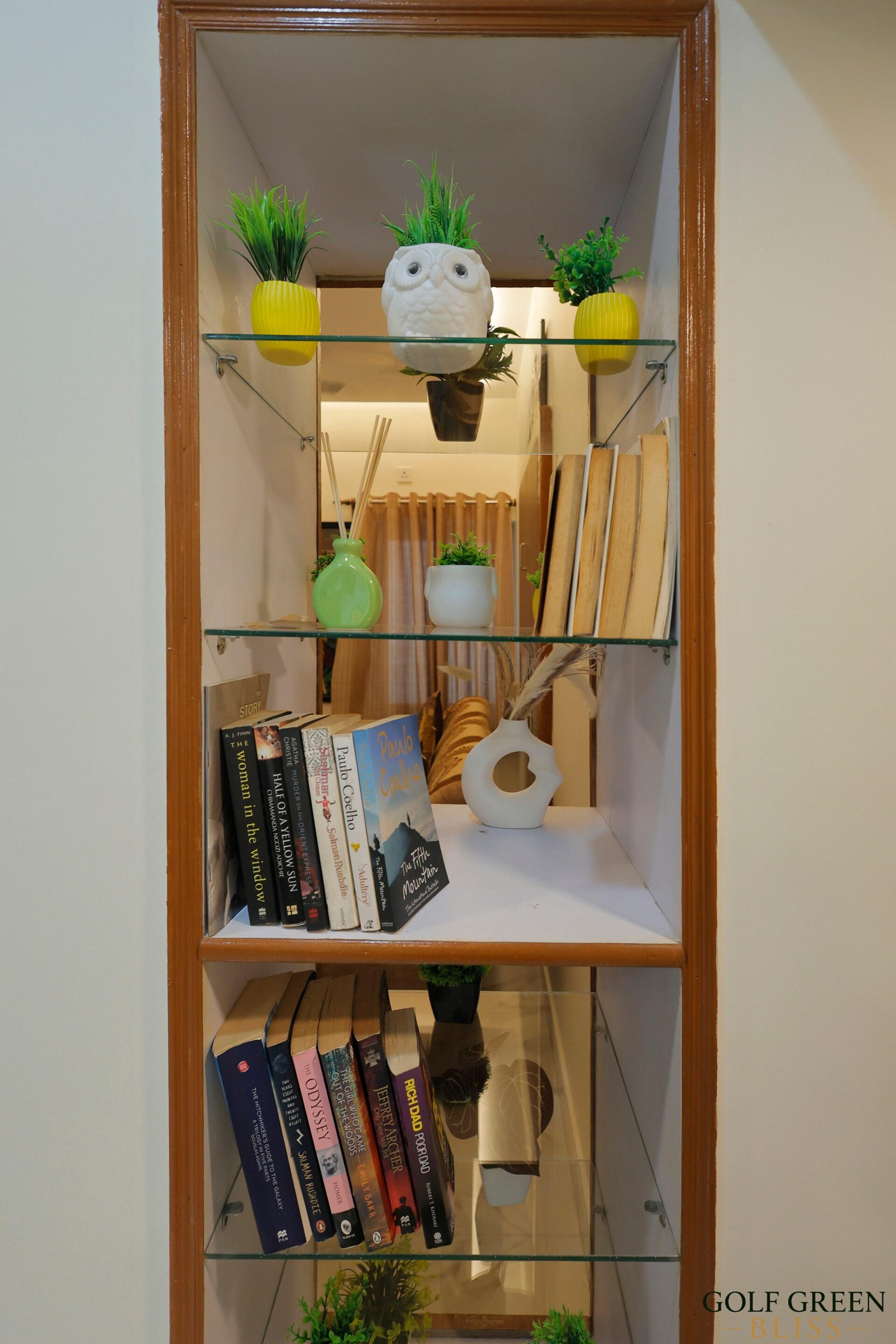 A glass-shelved bookcase holding books and small potted plants