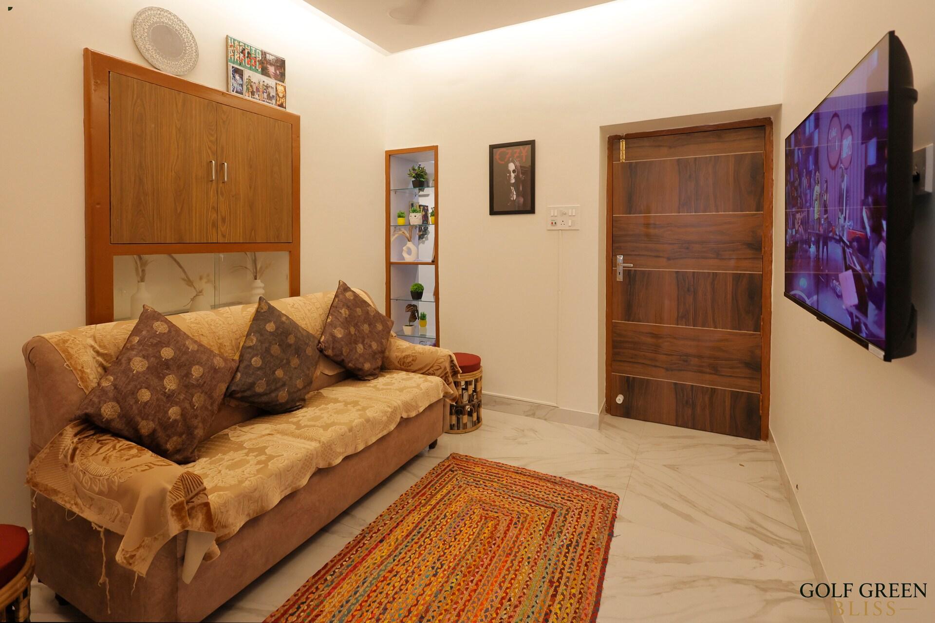 The living room with a cushioned sofa, wall-mounted television and a patterned rug on marble flooring