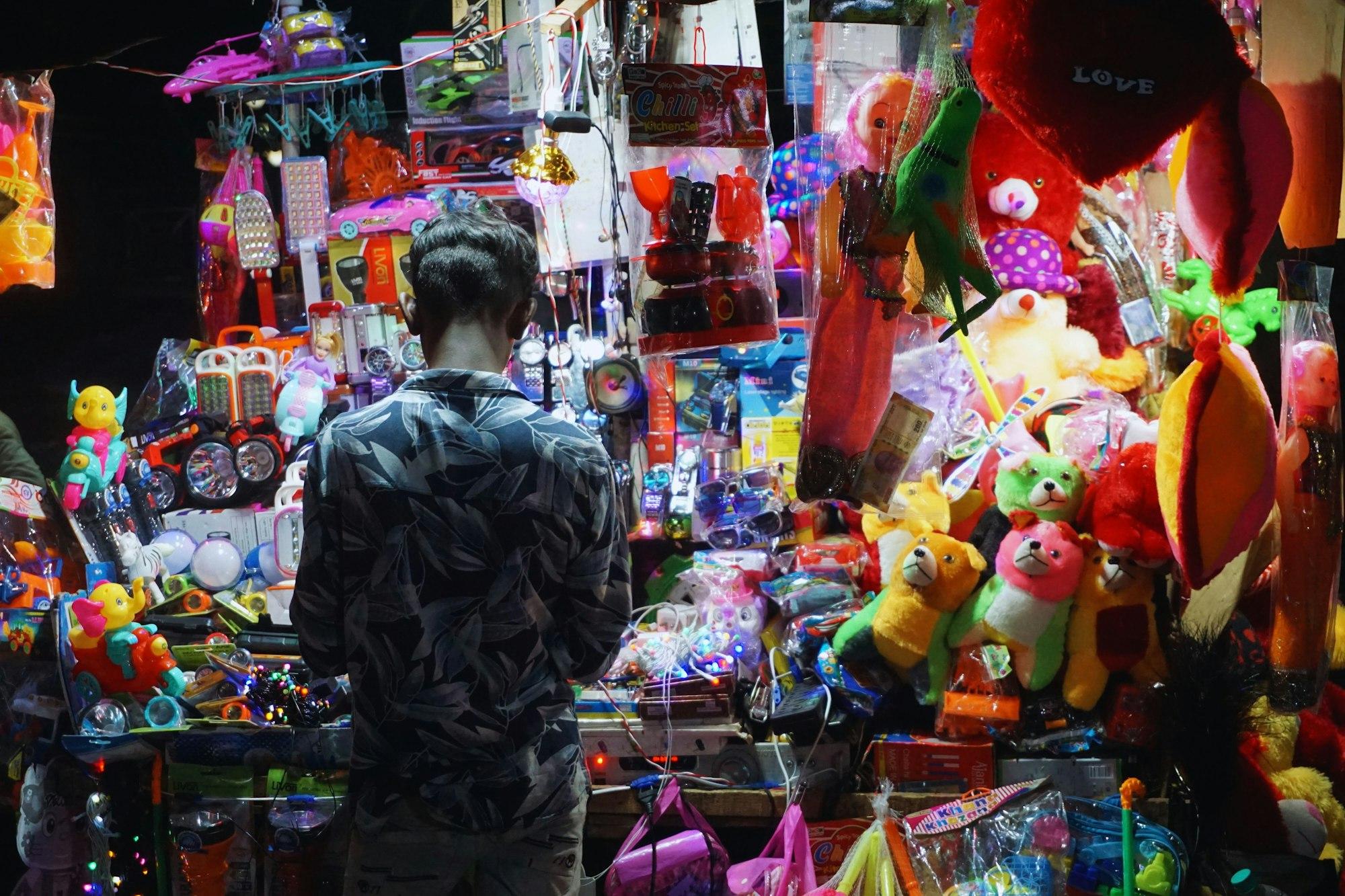 A person browsing a brightly lit street stall packed with colourful goods at night