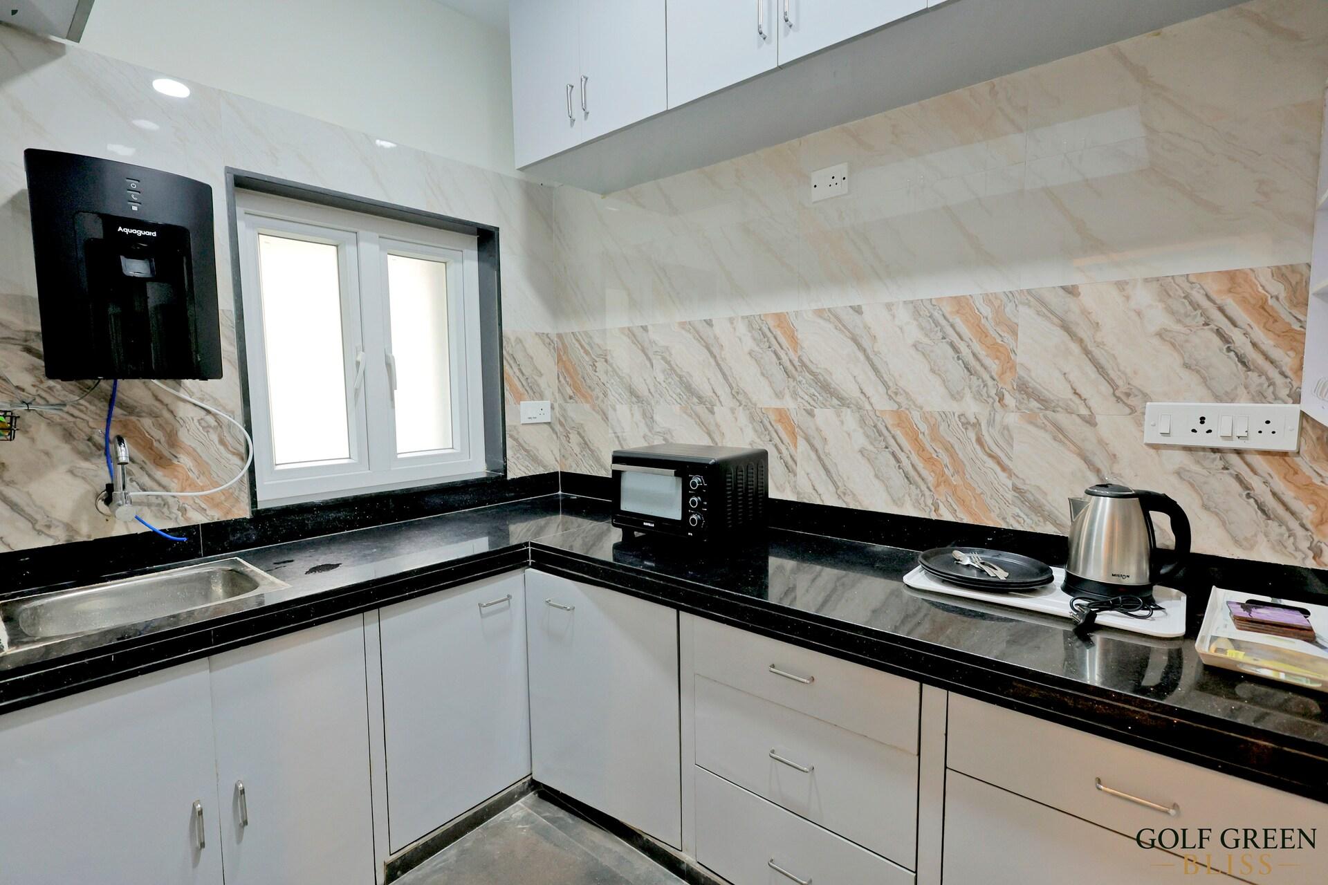 The kitchen with white cabinetry, a dark granite worktop, sink and electric kettle