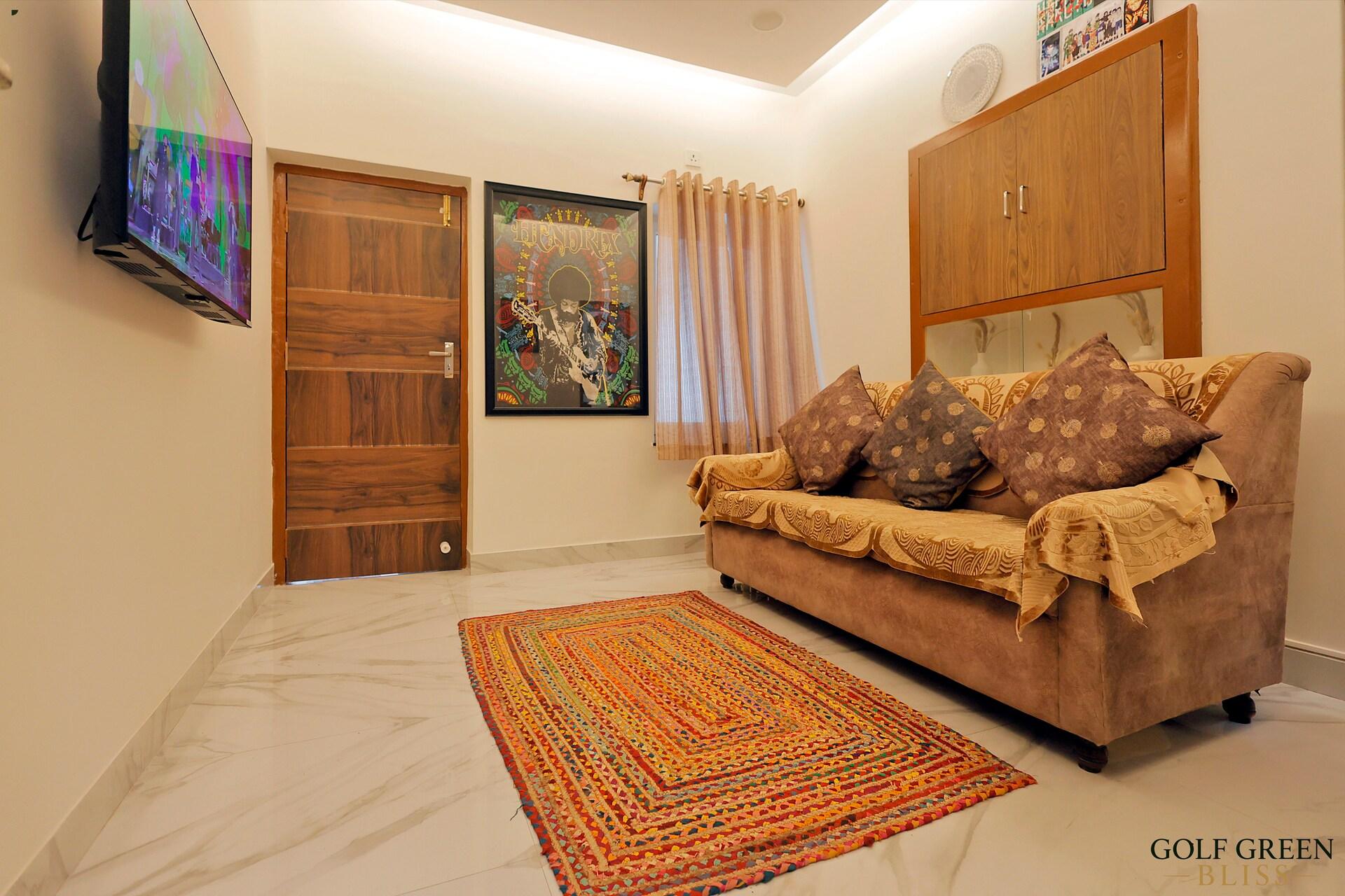 The living room with a cushioned sofa, wall-mounted television and a patterned rug on marble flooring