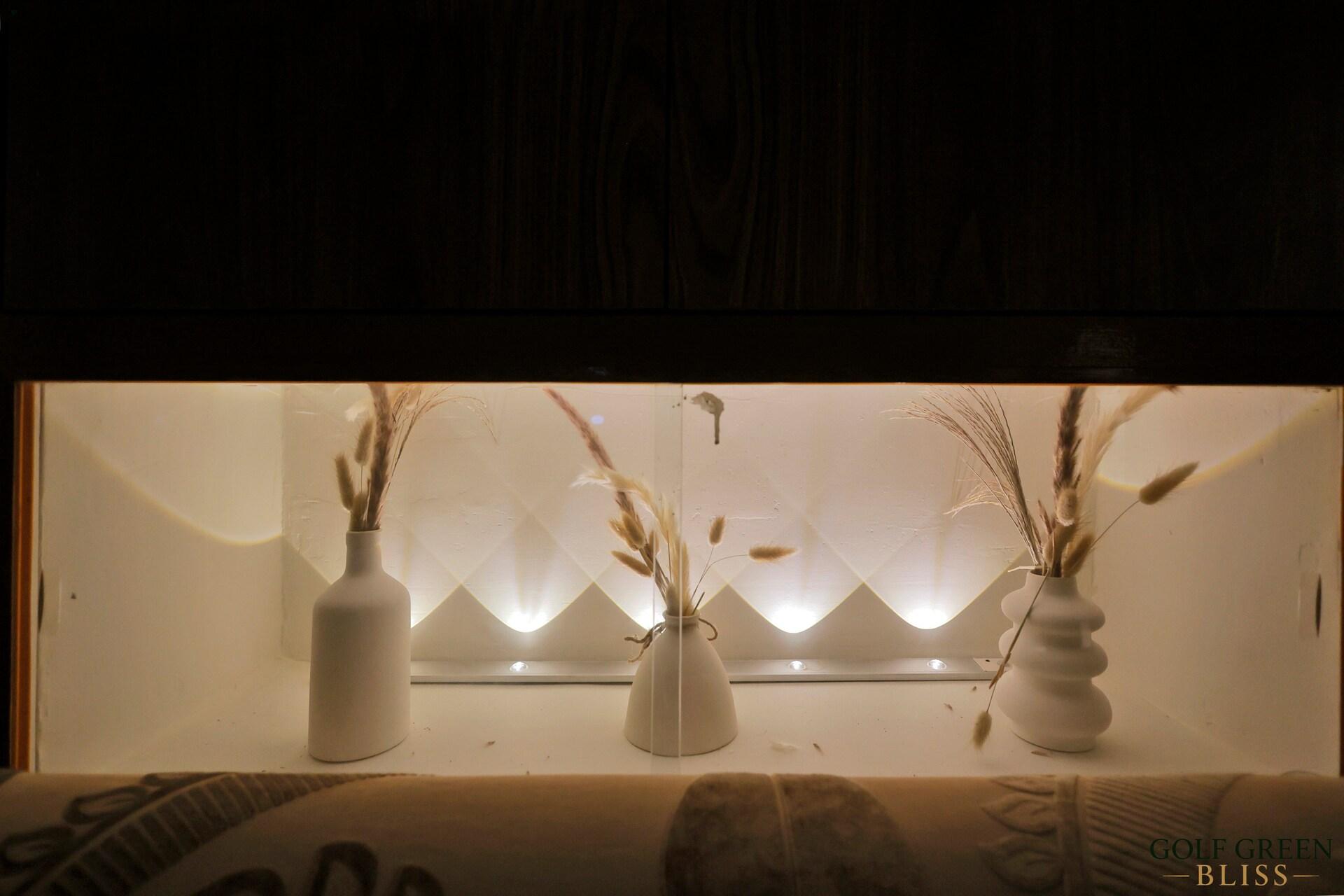 A lit display niche holding vases of dried stems